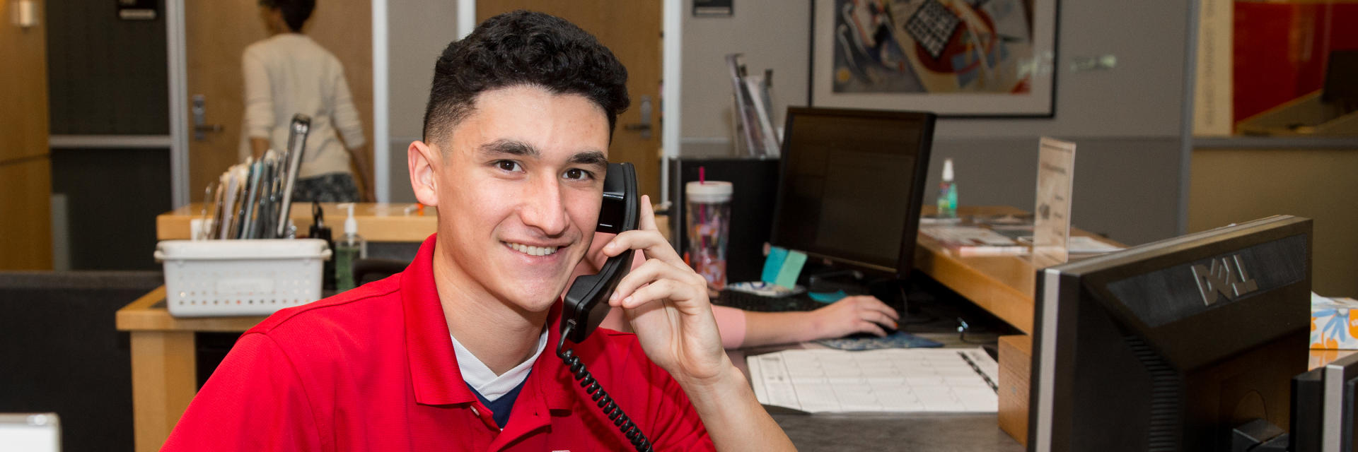 A male student faces the camera as he speaks on the phone and consults the computer