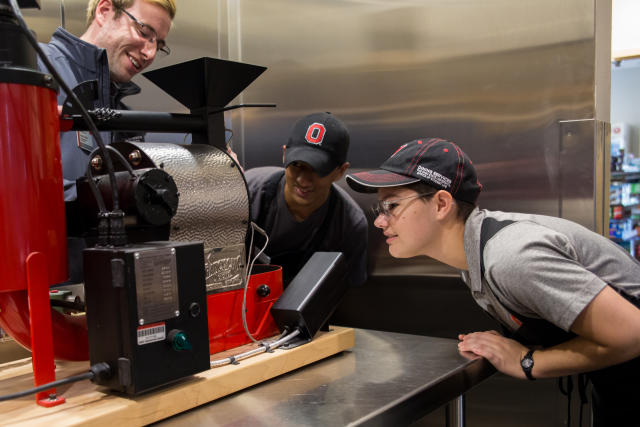 Two students and their supervisor watch as coffee is roasted